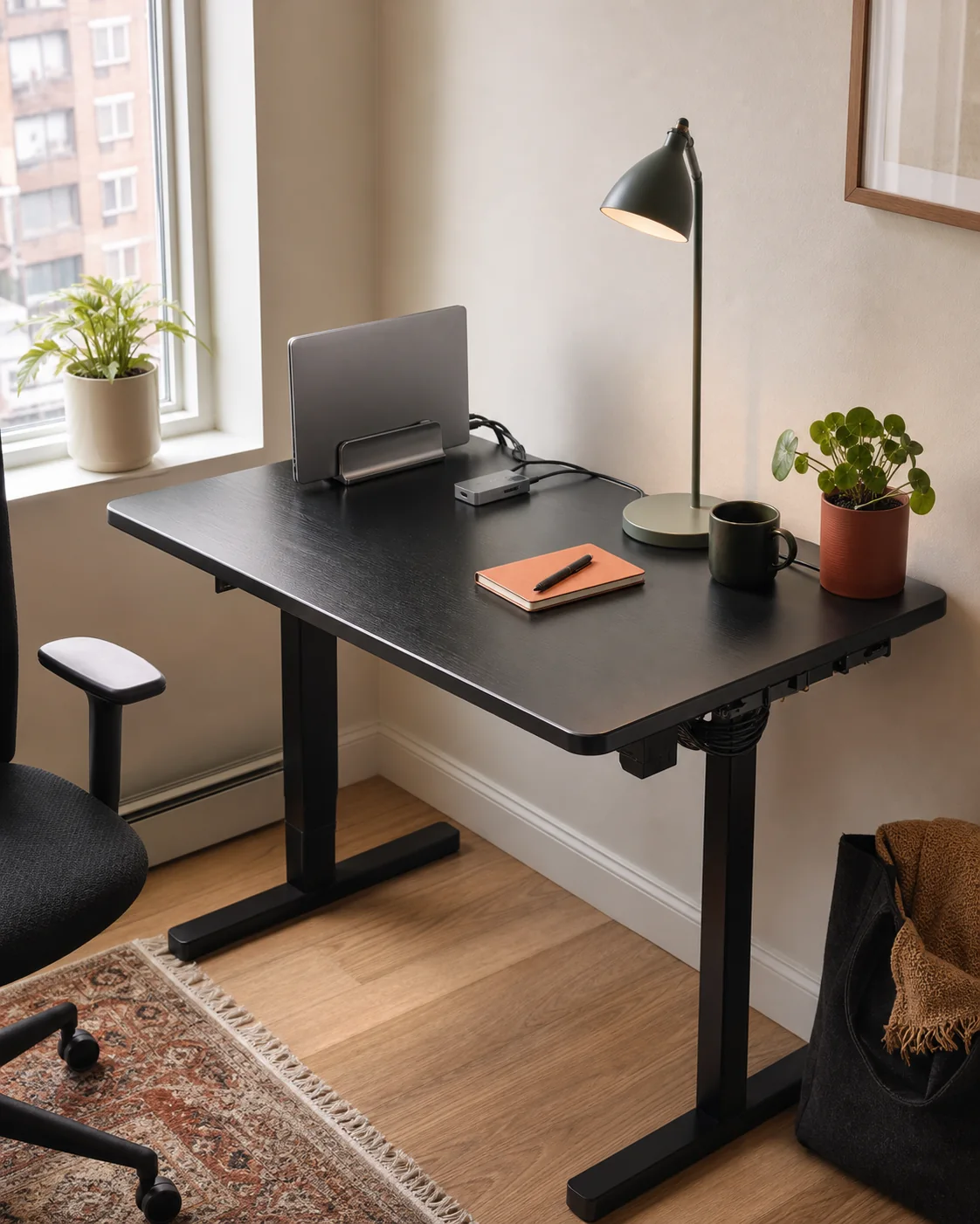 Compact apartment desk arranged with a vertical laptop stand, small hub, task light, and tidy cables