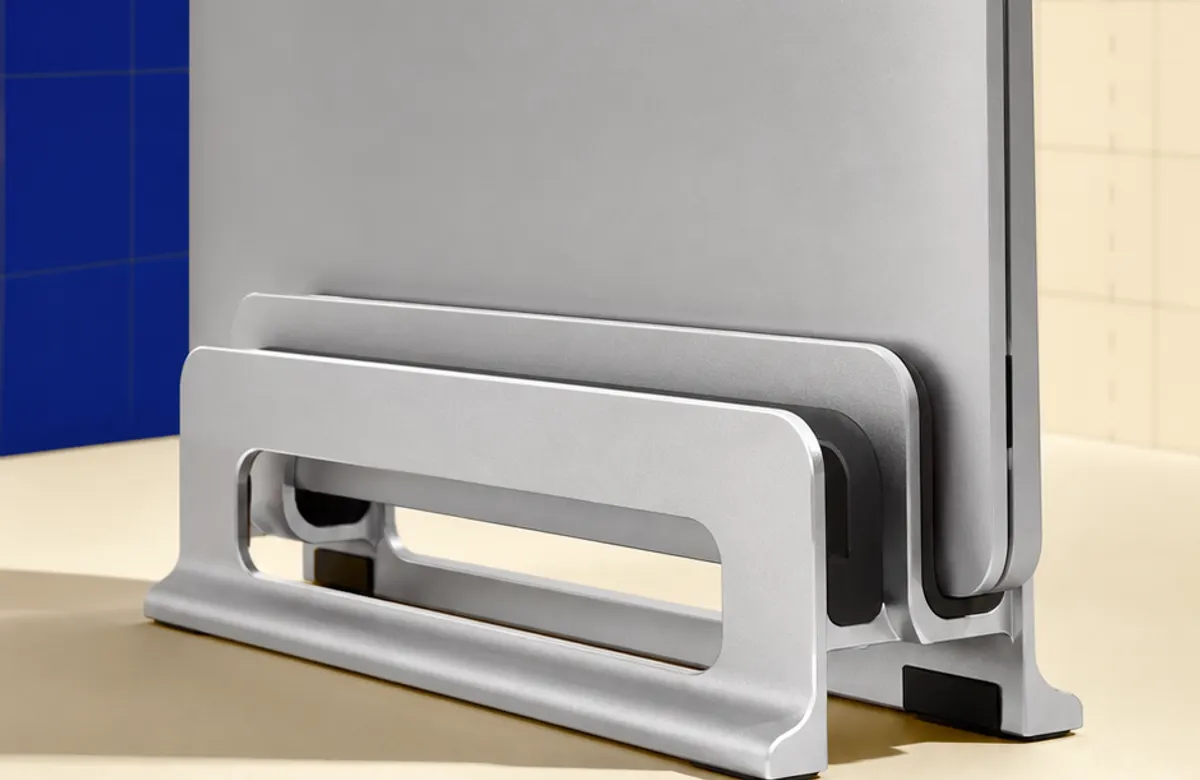 Original illustration of a closed laptop held upright in an adjustable-slot aluminium vertical stand on a desk